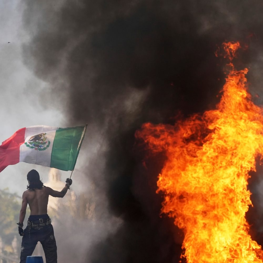 A protester waves a flag as a Waymo taxi burns near the Metropolitan Detention Center of downtown Los Angeles, Sunday, June 8, 2025, following last night's immigration raid protest. (AP Photo/Jae C. Hong) Alabama News