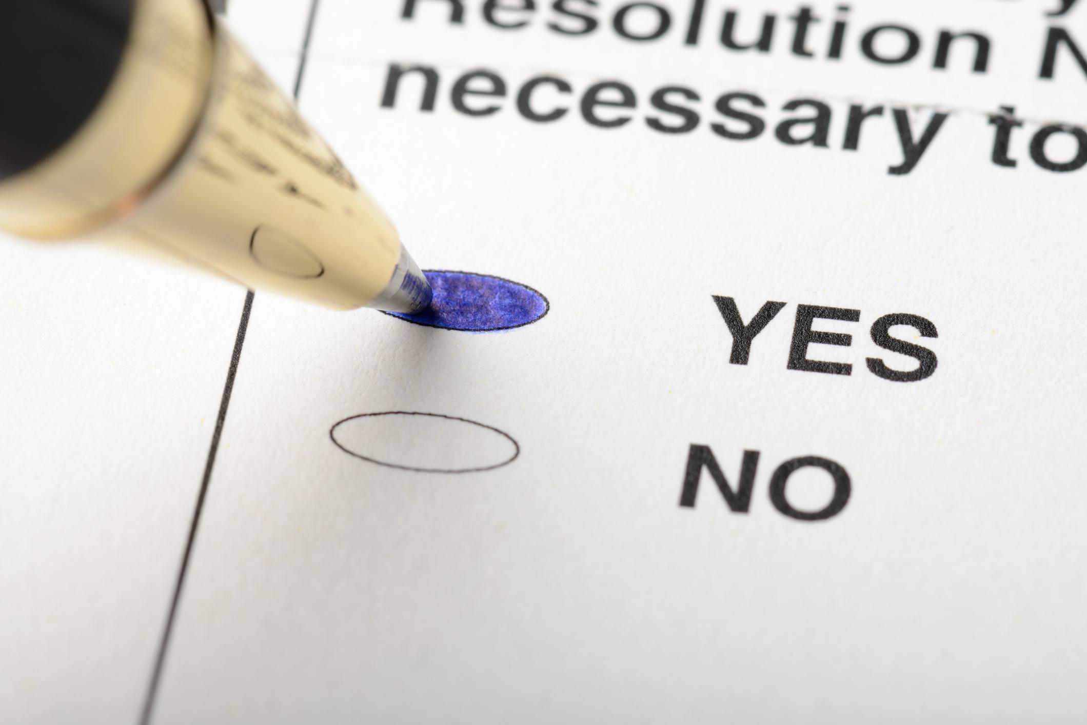 A close up of a pen filling in the yes option on a ballot.