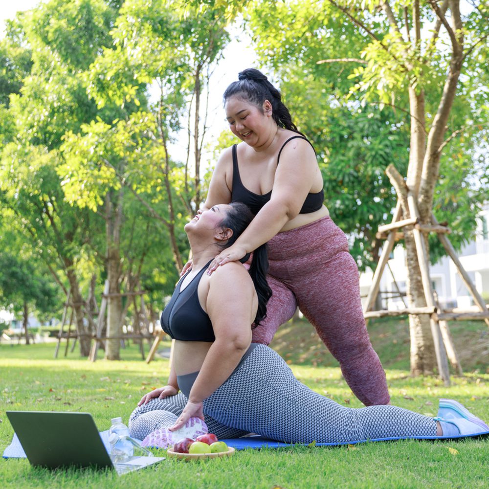 Asian female overweight in sportswear training exercise to lose weight on mat looking preview with laptop. woman plus size training online practice yoga in park. concept of healthy. stock photo Alabama News